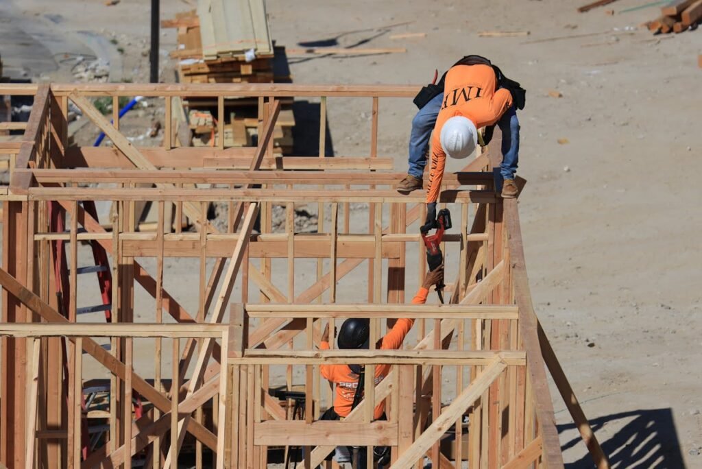 pexels-photo-17410515 Two construction workers framing a wooden structure outdoors at a building site.
