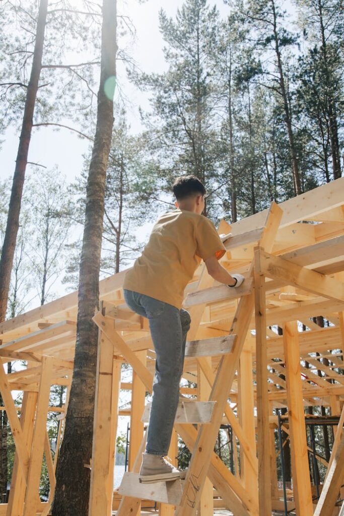 pexels-photo-8821558 A worker in a yellow shirt climbs a wooden ladder on an outdoor construction site.